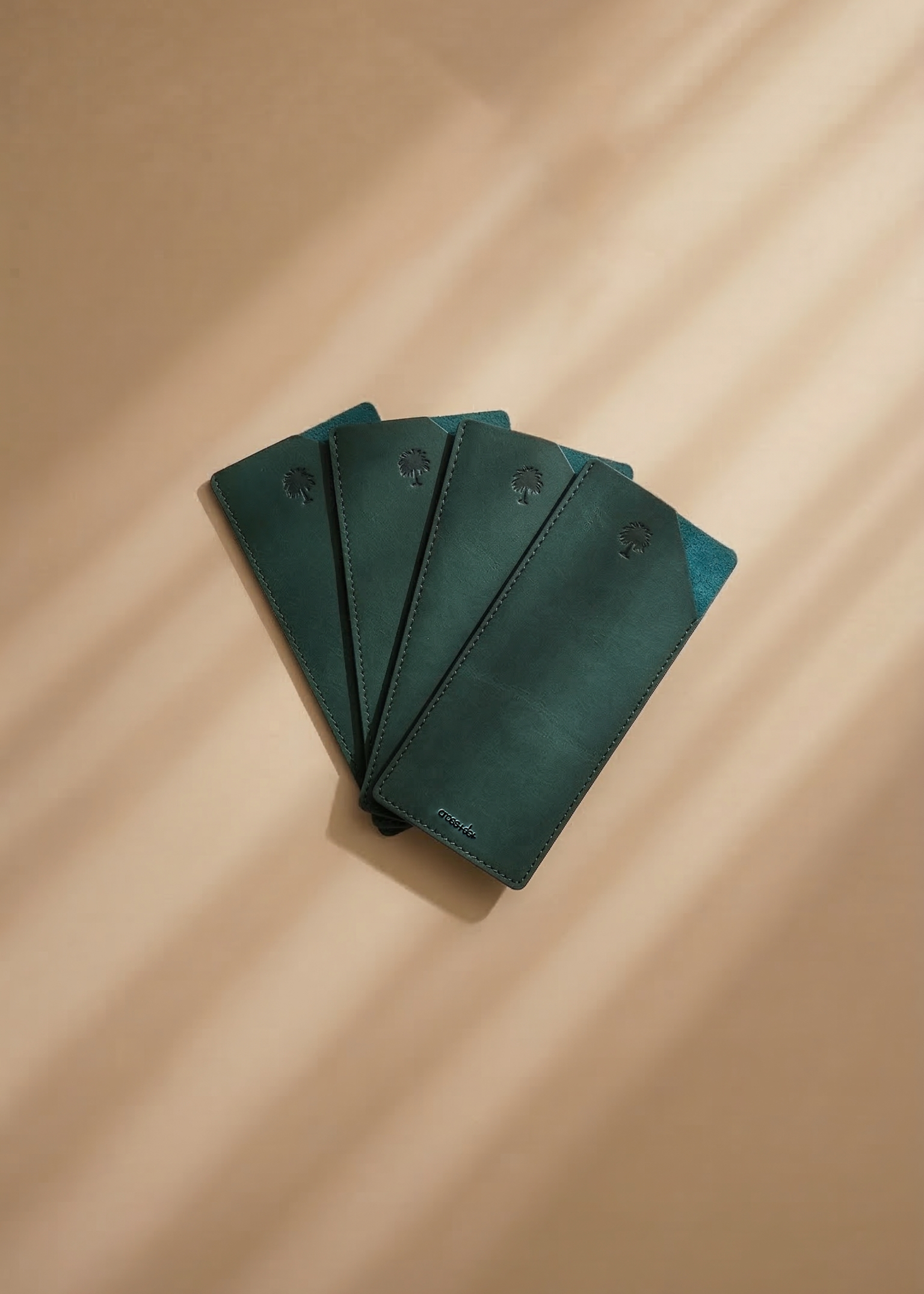 Set of green leather envelopes on a beige surface with soft shadows