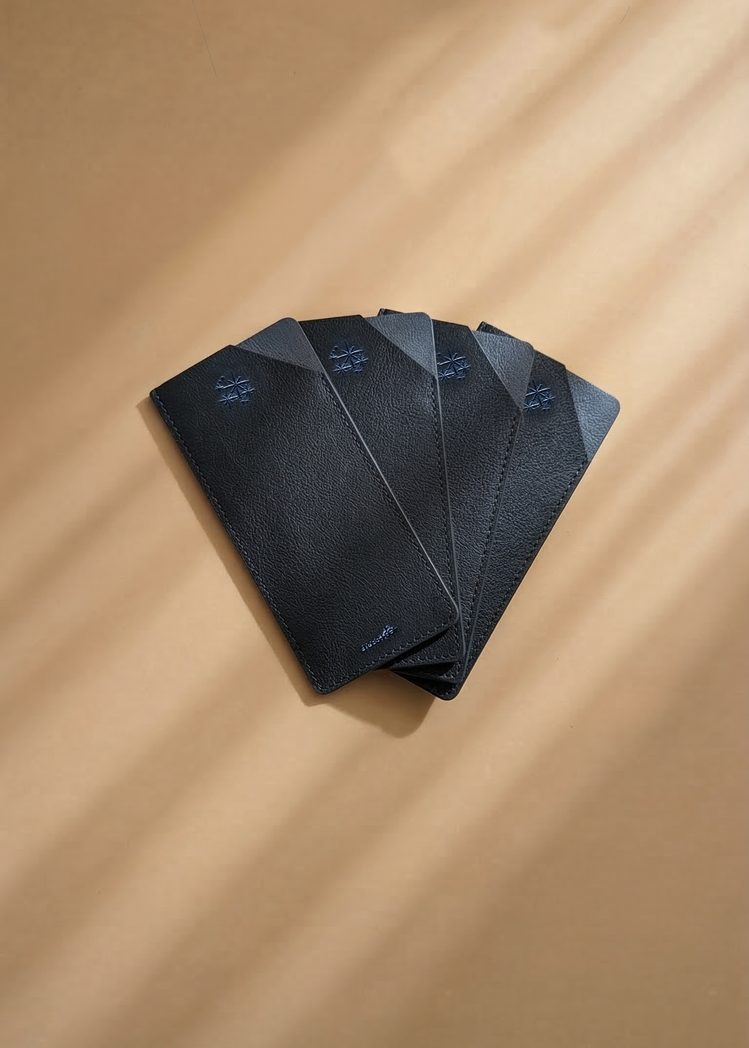 Four navy leather envelopes stacked on a beige surface with soft shadows
