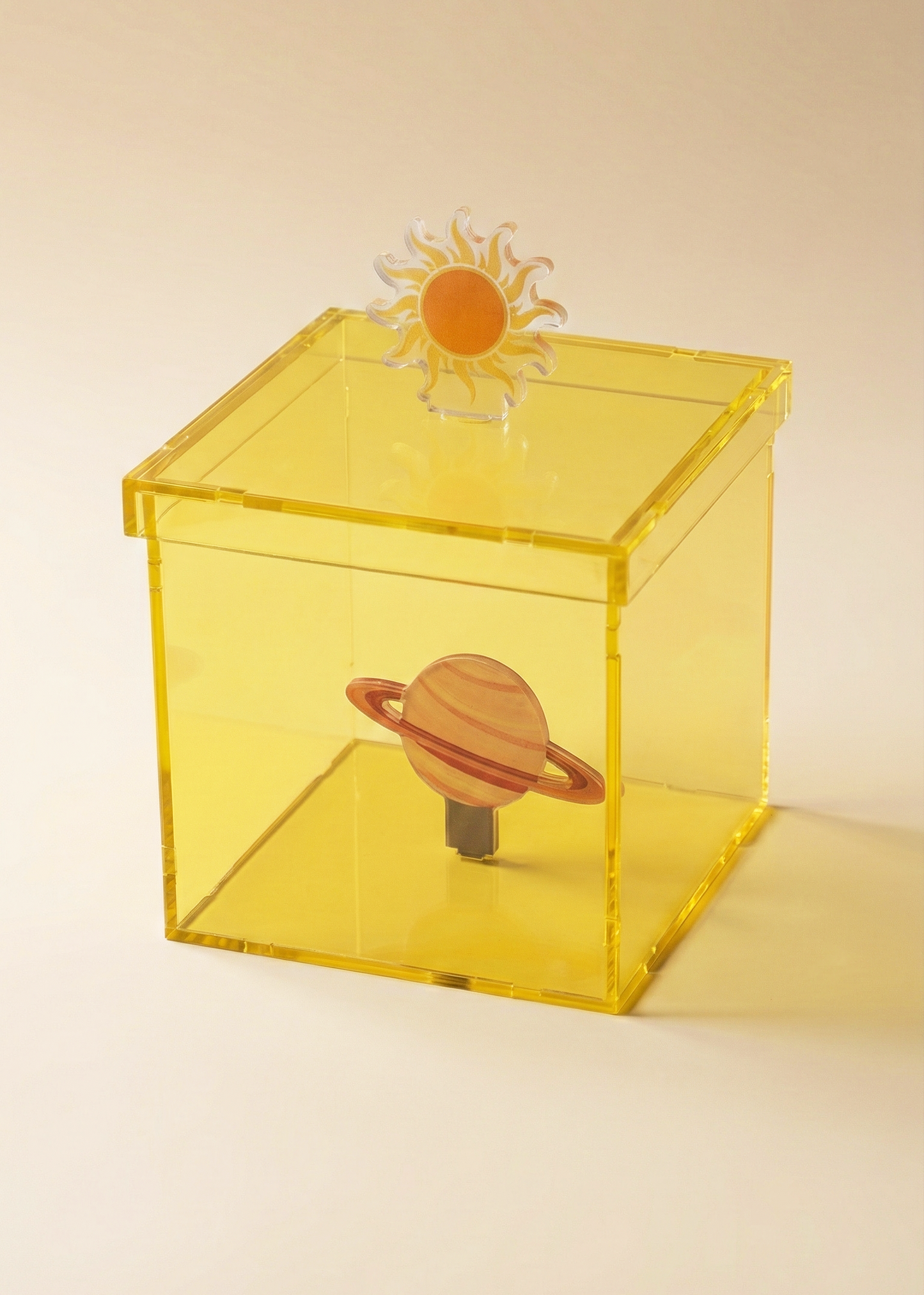 Yellow transparent box with solar system-themed objects on a beige background
