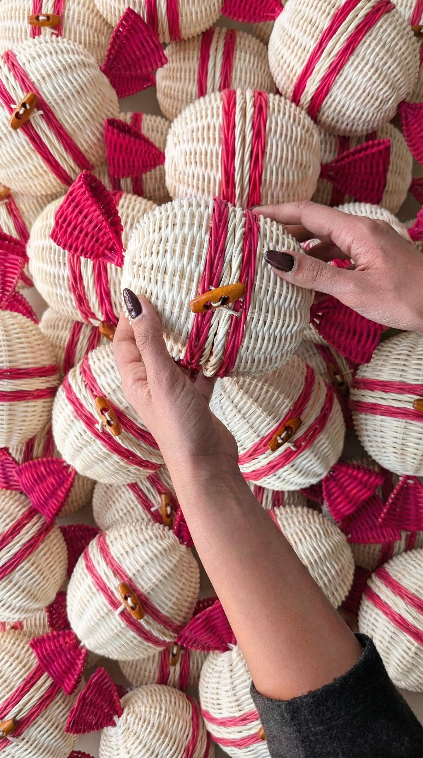 Woven candy shaped parcels beige and red being held by a person against a background of similar parcels